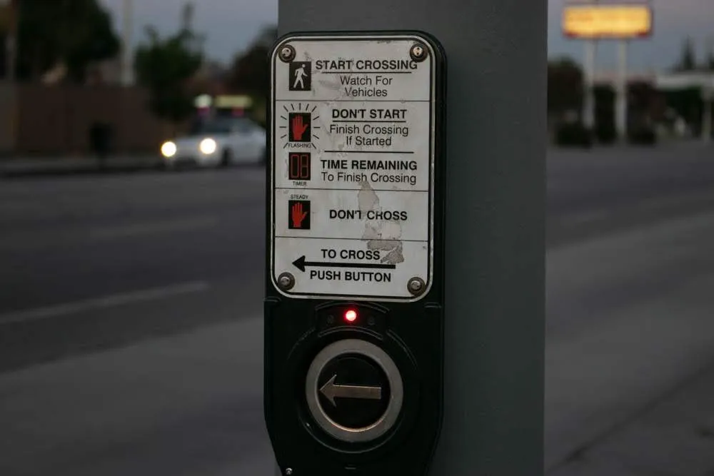 A pedestrian crossing signal button beside a roadway at dusk