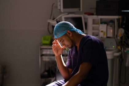 surgeon-sitting-with-his-head-in-his-hand-in-SHNZ4QU