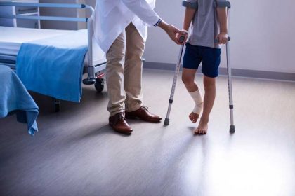 doctor-assisting-injured-boy-to-walk-with-crutches-3YFKCH6